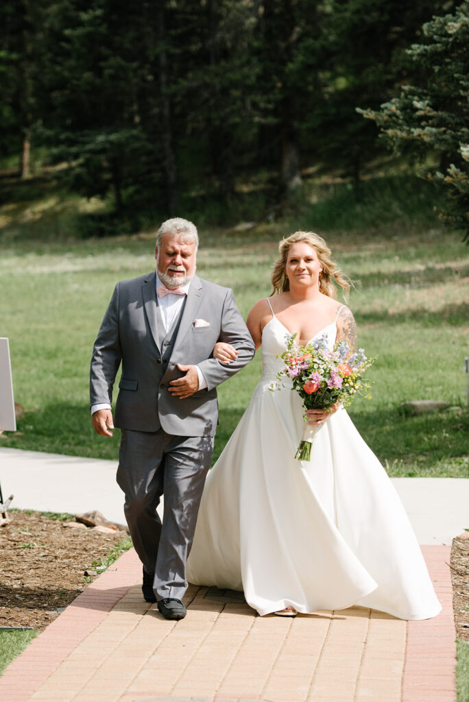 Ceremony placing take outdoors at Wedgewood Mountain View Ranch in Pine, CO with mountain views and a rustic wooden arbor.