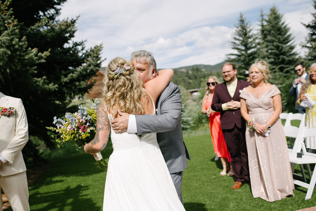 Ceremony placing take outdoors at Wedgewood Mountain View Ranch in Pine, CO with mountain views and a rustic wooden arbor.