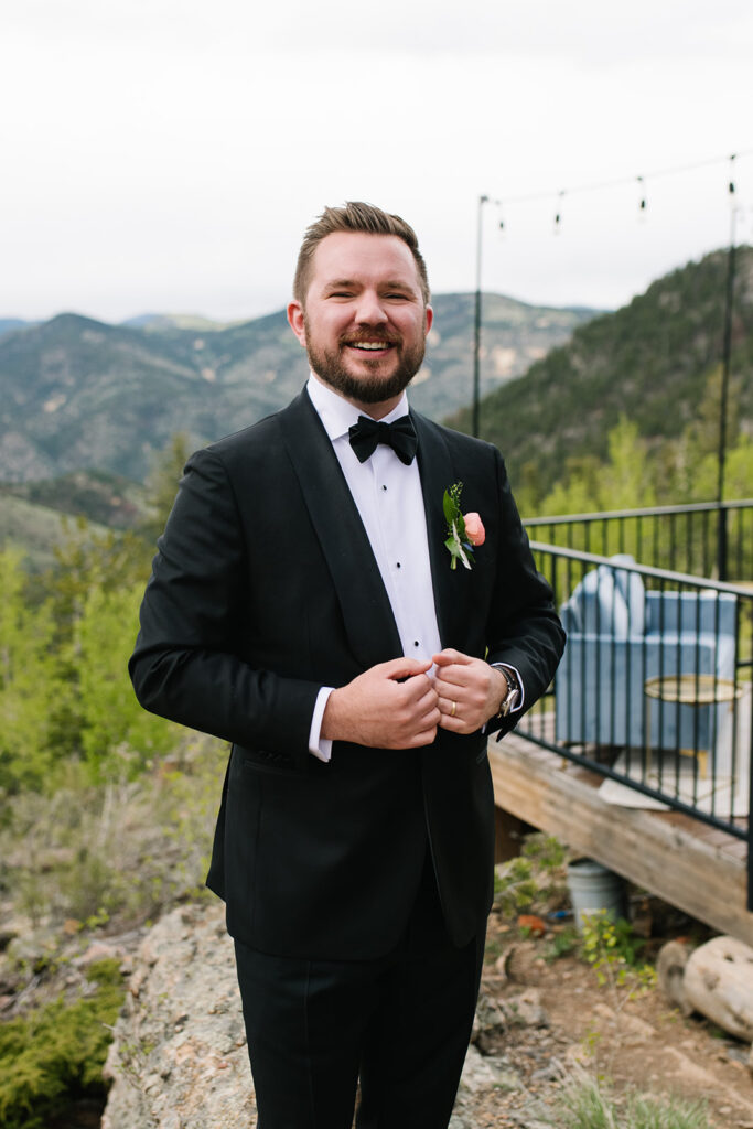 groom standing on ceremony deck at North Star Gatherings in Idaho Springs with mountain views behind them.